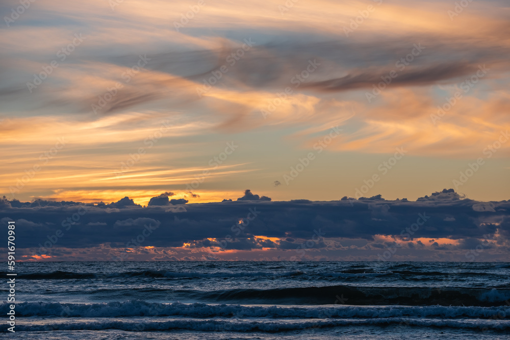 Dramatic sunset in the sea. The sea, dark clouds like a mountain range above the horizon, the sun behind the clouds. Blurry clouds in the sky in the background. Copy space. Background for quotes.