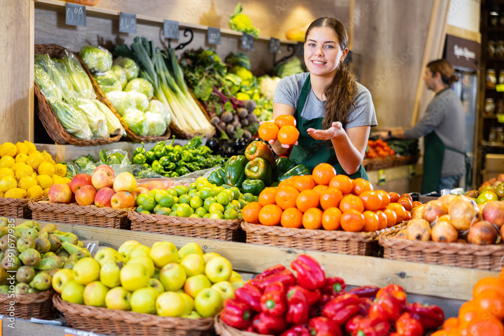 Saleswoman near fruit and vegetables stalls offering to buy mandarin oranges