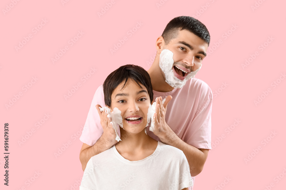 Man and his little son applying shaving foam onto faces against pink background