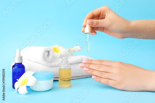 Woman applying oil onto cuticles on color background