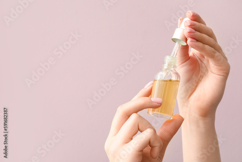 Female hands with bottle of cuticle oil against color background, closeup photo