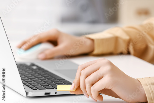 Woman working with modern laptop and USB flash drive at light table, closeup