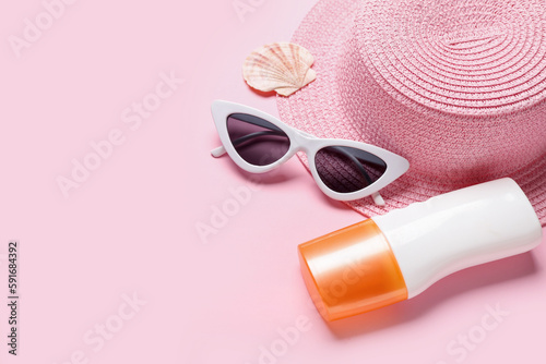 Bottle of sunscreen cream, hat, sunglasses and seashell on pink background. Melanoma concept