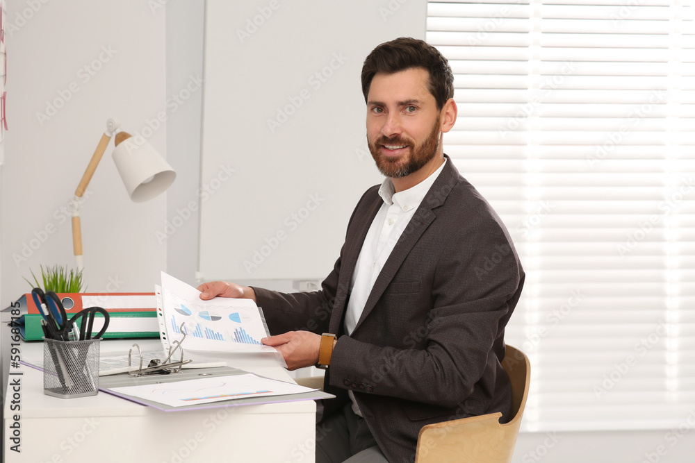 Businessman putting document into punched pocket at white table in office Businessman putting document into punched pocket at white table in office