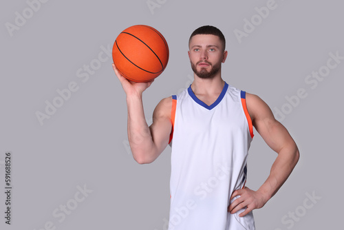 Athletic young man with basketball ball on light grey background. Space for text