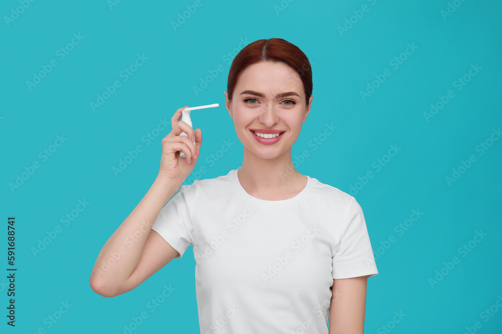 Woman using ear spray on light blue background Woman using ear spray on light blue background