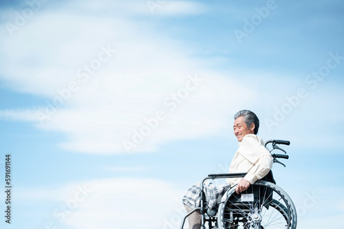 青空をバックに車椅子に乗るシニア男性