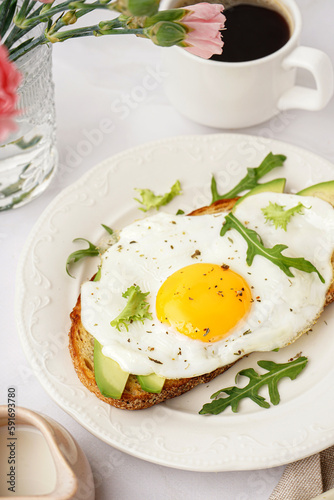Delicious sandwich with fried egg, avocado and arugula on light background