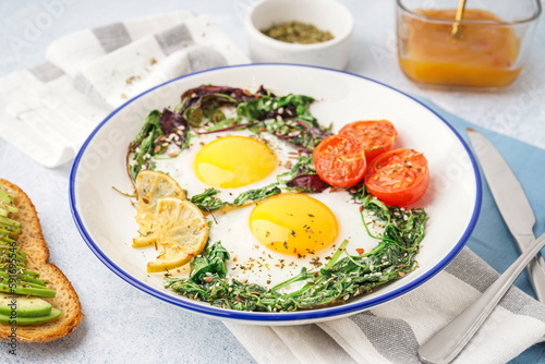 Plate with tasty fried eggs, salad and avocado sandwich on light background