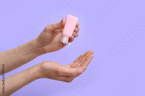 Woman applying sanitizer on lilac background