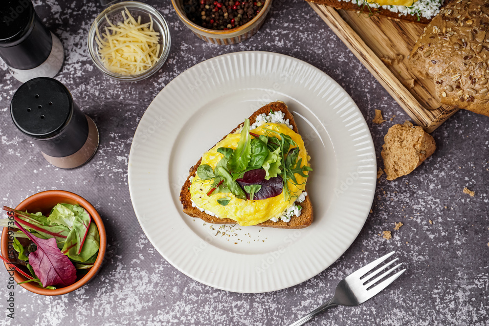 Plate with tasty scrambled eggs sandwich on grey grunge background