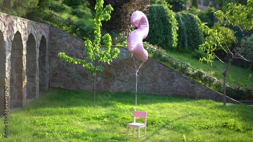A pink balloon with the number two flies over a small pink chair 4K photo