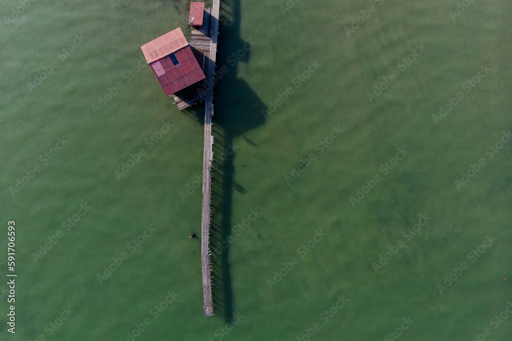 Aerial top down view of a long wooden dock with a small red colour zinc roof wooden houses on green colour sea as background