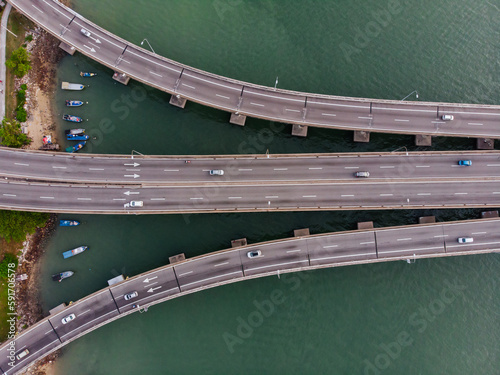 Aerial top down view of the beginnig of the bridge with the shore, fishing boat and greenish colour sea water background.
