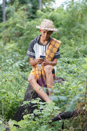 Rural man sitting on tree trunk holding smartphone in the forest