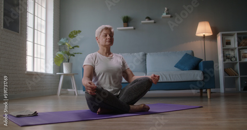 Mature caucasian woman doing yoga at home. Senior woman relaxing in lotus position on floor, keeping a healthy lifestyle - wellness concept 