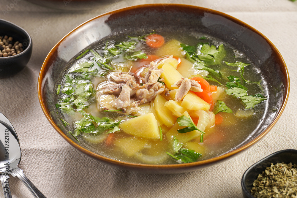 two deep green bowls with traditional european chicken soup with potato, carrots, celery, fresh parsley on a beige colored kitchen table cloth two deep green bowls with traditional european chicken soup with potato, carrots, celery, fresh parsley on a beige colored kitchen table cloth