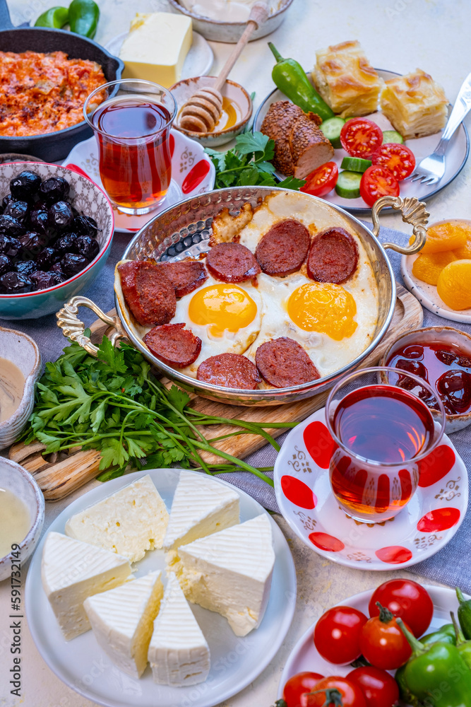 Turkish breakfast table from front view. Eggs and sujuk in a copper pan. Olives, cheese and Turkish tea in tulip glasses around it. Turkish breakfast table from front view. Eggs and sujuk in a copper pan. Olives, cheese and Turkish tea in tulip glasses around it.