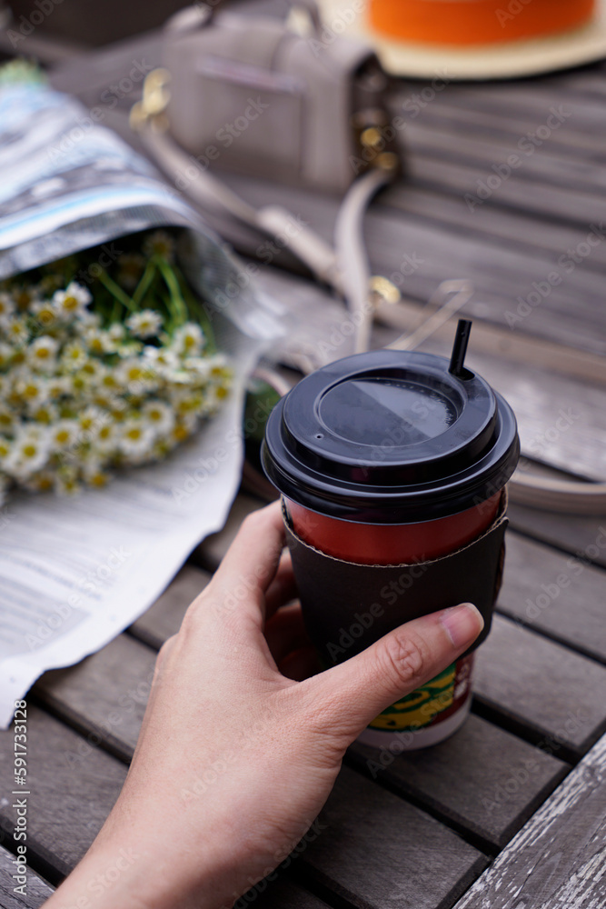 Cropped hand holding a take away coffee cup on wooden table outdoor Cropped hand holding a take away coffee cup on wooden table outdoor