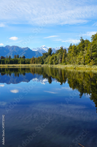 Clear mirror Lake Matheson under a blue sky reflecting Aoraki Mount Cook and Mount Tasman in Fox Glacier