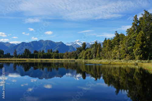 Clear mirror Lake Matheson under a blue sky reflecting Aoraki Mount Cook and Mount Tasman in Fox Glacier