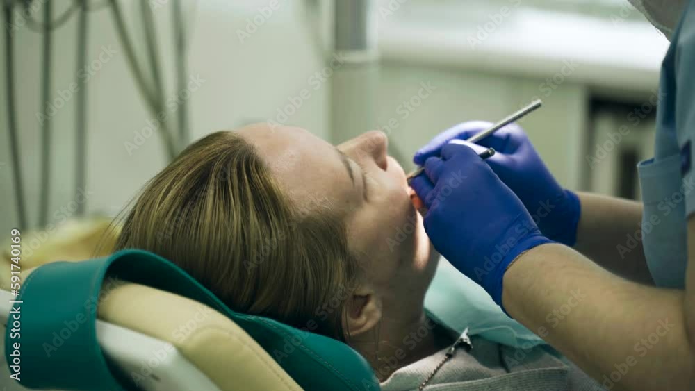 A doctor examines a woman's teeth with a dental instrument. Close-up A doctor examines a woman's teeth with a dental instrument. Close-up