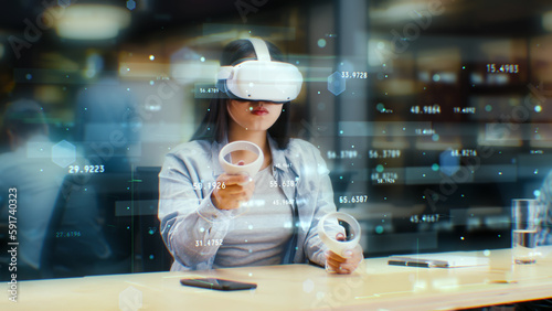 Female office worker uses VR headset and wireless controllers, watches data and numbers in 3D virtual reality. Asian woman works in modern hi-tech IT company. Future innovative digital technologies.