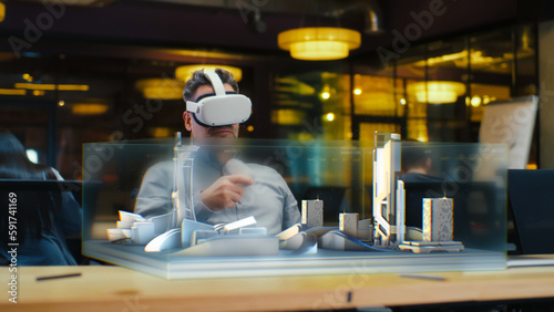 Male architect uses VR headset and wireless controllers, creates architectural project of metropolis in virtual reality. Man works in hi-tech company. 3D hologram. Future innovative AI technologies.