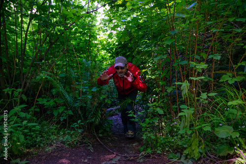 Adventurous athletic man acting funny as he walks out of the bushes covering a hiking trail on the rugged coastline of the Pacific Northwest. 