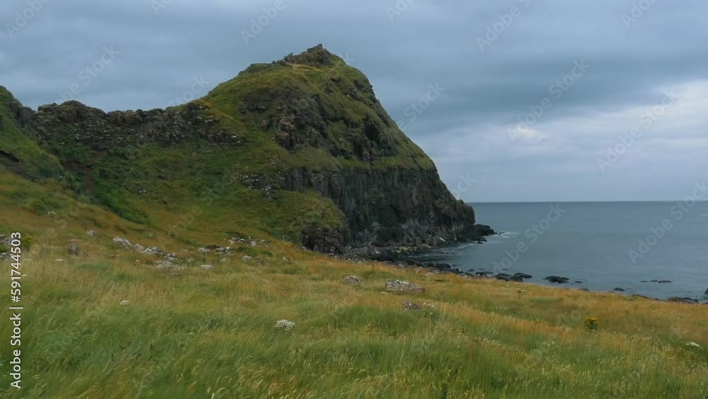 Beautiful Northern Ireland landscape. A green plain that slants up to a hill on the left and the North Atlantic Ocean on the right. Slow motion, cinematic. Beautiful Northern Ireland landscape. A green plain that slants up to a hill on the left and the North Atlantic Ocean on the right. Slow motion, cinematic.
