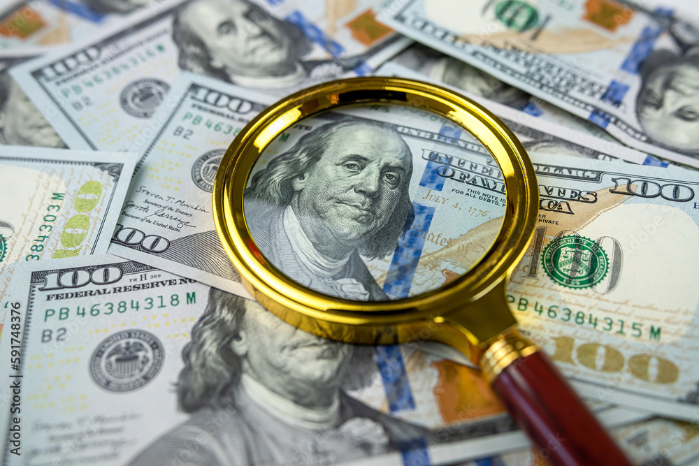Closeup one hundred US dollar bills under gold magnifying glass Closeup one hundred US dollar bills under gold magnifying glass