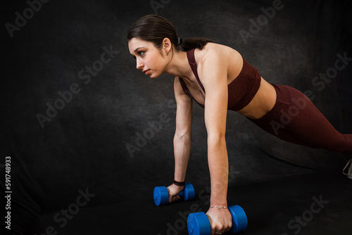 Pretty slim woman wear sport cloth does the exercises with dumbbells isolated on black