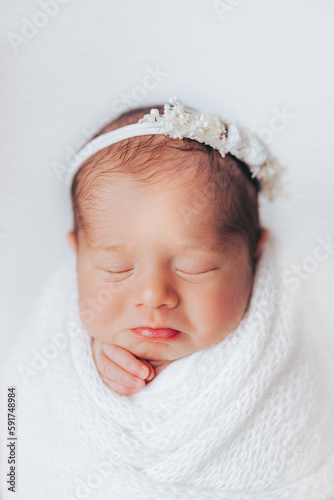 Newborn baby girl photographed in studio, on white background. Stylized and wrapped. Cute expression.