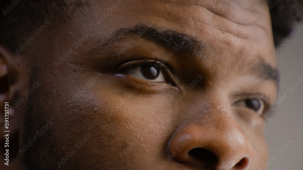 Detailed portrait of young African American man straight and serious face with confident look. Concentrated guy looks away, blinks eyes, poses on camera. Man stands in studio on the grey background. Detailed portrait of young African American man straight and serious face with confident look. Concentrated guy looks away, blinks eyes, poses on camera. Man stands in studio on the grey background.