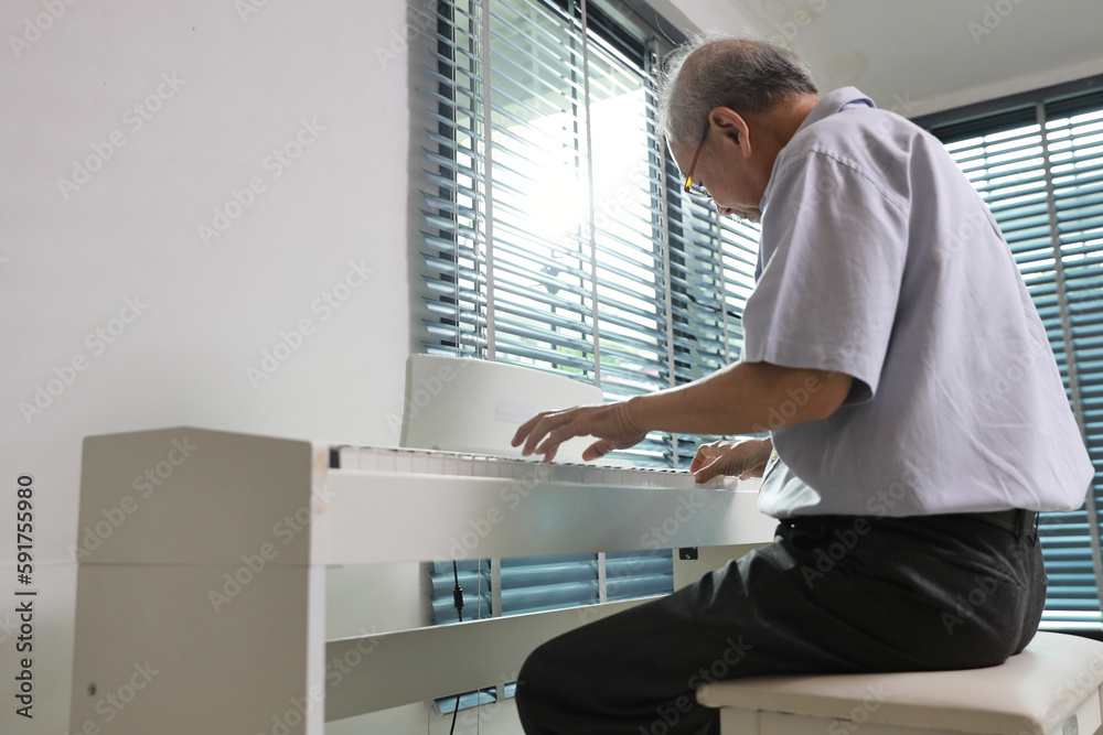 Happy smiling asian senior man with beard sitting and playing piano and singing a song in living room house indorrs. Musical and relaxation makes elder male happiness. Health care lifestyle concept.