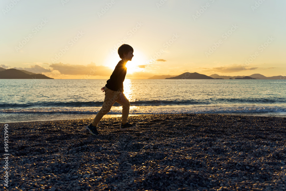 Silhouette of little boy on the beach at sunset.