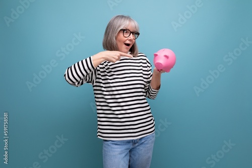 Foto cute grandmother old woman 50s holding a piggy bank with a pension on a bright b