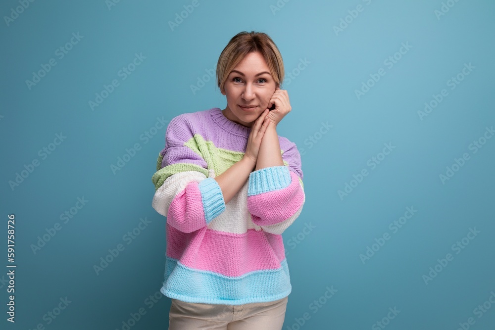 close-up of a shy blond young woman in a casual outfit on a blue background with copy space