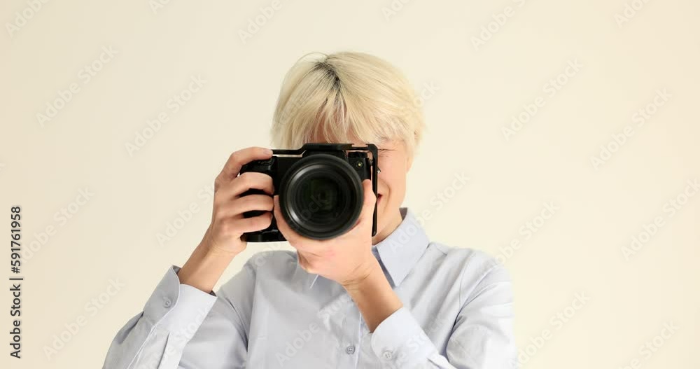 Young woman with dyed blonde hair takes photos with professional camera. Skilled photographer points modern device to camera smiling slow motion Young woman with dyed blonde hair takes photos with professional camera. Skilled photographer points modern device to camera smiling slow motion
