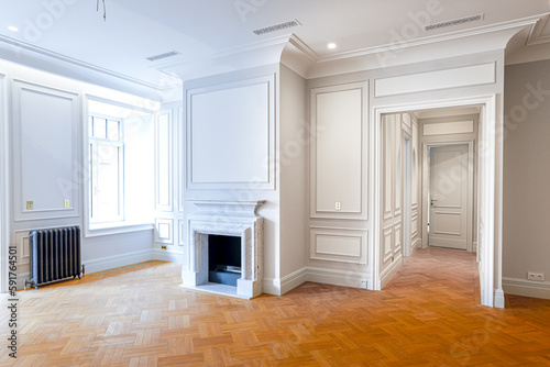 interior of an empty room with white walls with paneling, wooden parquet and a fireplace