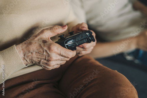 Senior woman playing with modern technology gadget using video games console on television. Caucasian gamer with wireless controller sitting at home. People