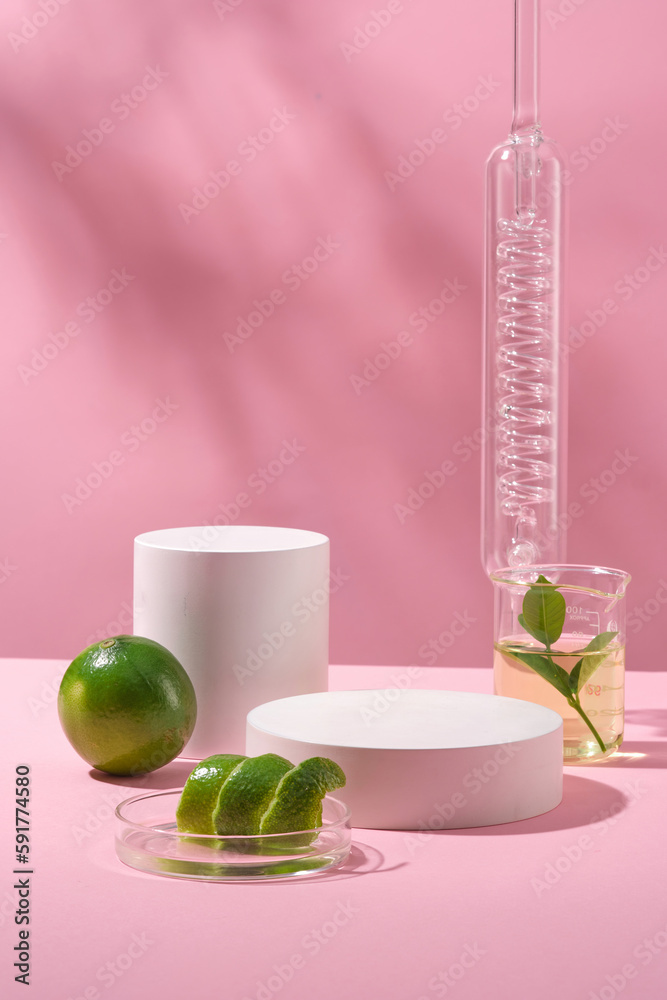 Background for the presentation of cosmetic products with white cylinder podium, lime, peel in petri dish and liquid in beaker, on pink background with natural shadow leaves. Front view, copy space.