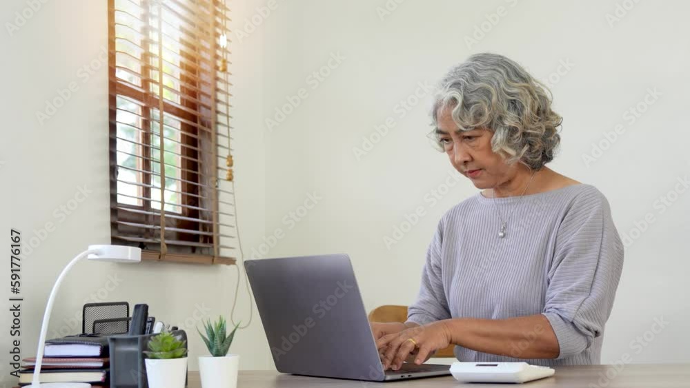 elderly woman sitting at room table and working on laptop computer elderly woman sitting at room table and working on laptop computer