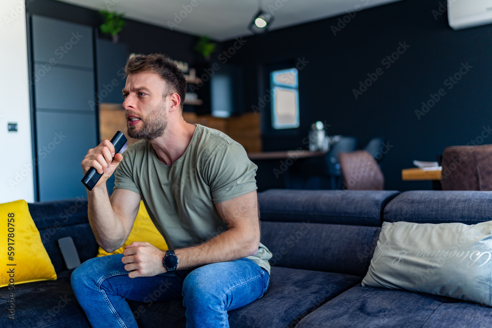 the young man is tense while watching the game, on the edge of the couch holding the remote control in his hand and getting annoyed the young man is tense while watching the game, on the edge of the couch holding the remote control in his hand and getting annoyed