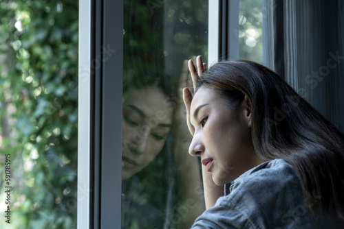 Portrait of sad and worried Asian woman looking through the window at home