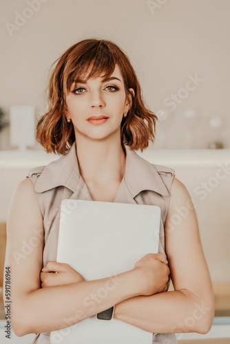 Brunette macbook. Portrait of a woman, she holds a mabuk in her hands and looks at the camera, wearing a beige dress on a beige background. photo