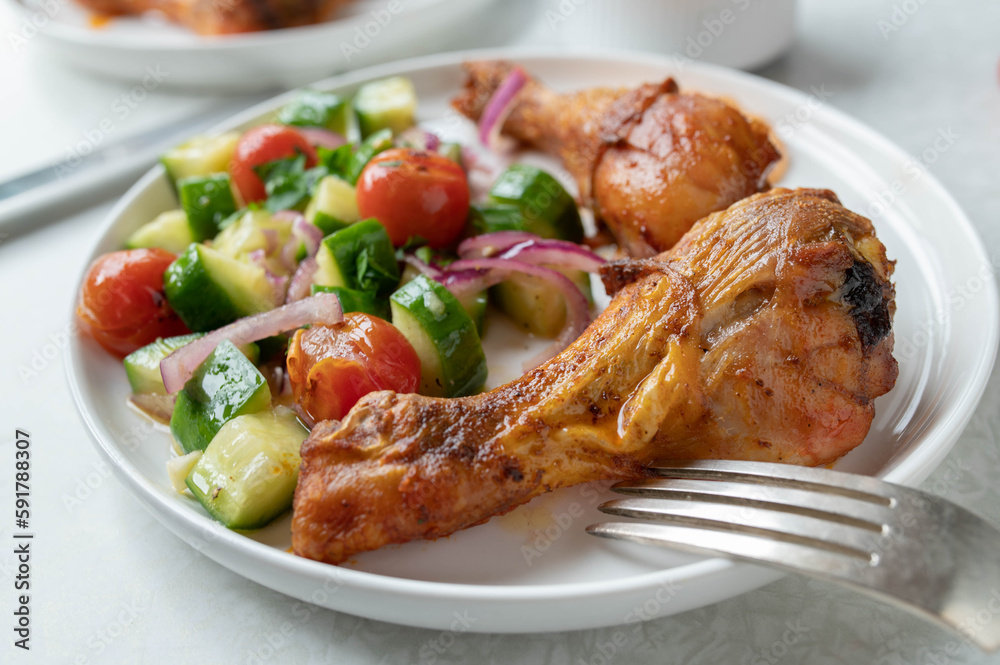 Oven baked chicken drumsticks with cucumber tomato salad on a plate Oven baked chicken drumsticks with cucumber tomato salad on a plate