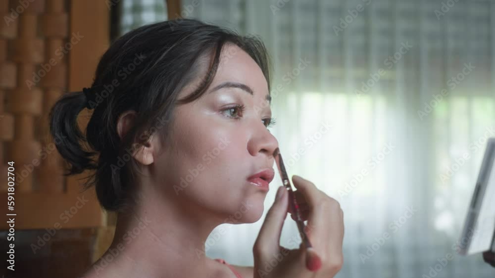 Beautiful Korean girl applying make-up on face. Asian woman making contour of nose using a make up brush and dark powder. Bronzer for shades. Morning routine of pretty female at home. Beauty treatment Beautiful Korean girl applying make-up on face. Asian woman making contour of nose using a make up brush and dark powder. Bronzer for shades. Morning routine of pretty female at home. Beauty treatment