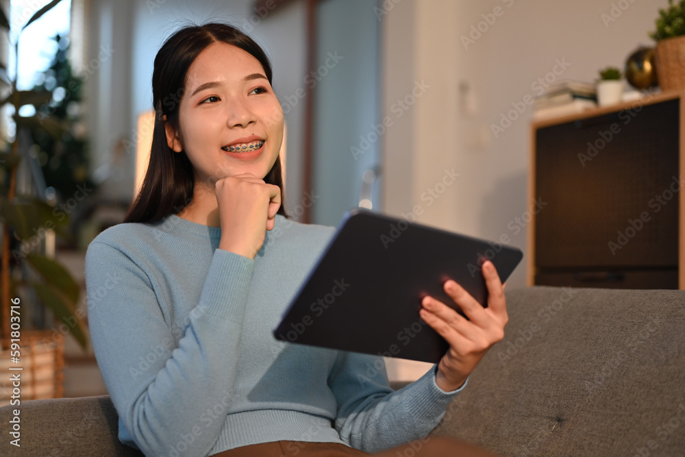 Smiling adult woman sitting on couch browsing wireless internet on digital tablet. Technology, people and lifestyle concept Smiling adult woman sitting on couch browsing wireless internet on digital tablet. Technology, people and lifestyle concept