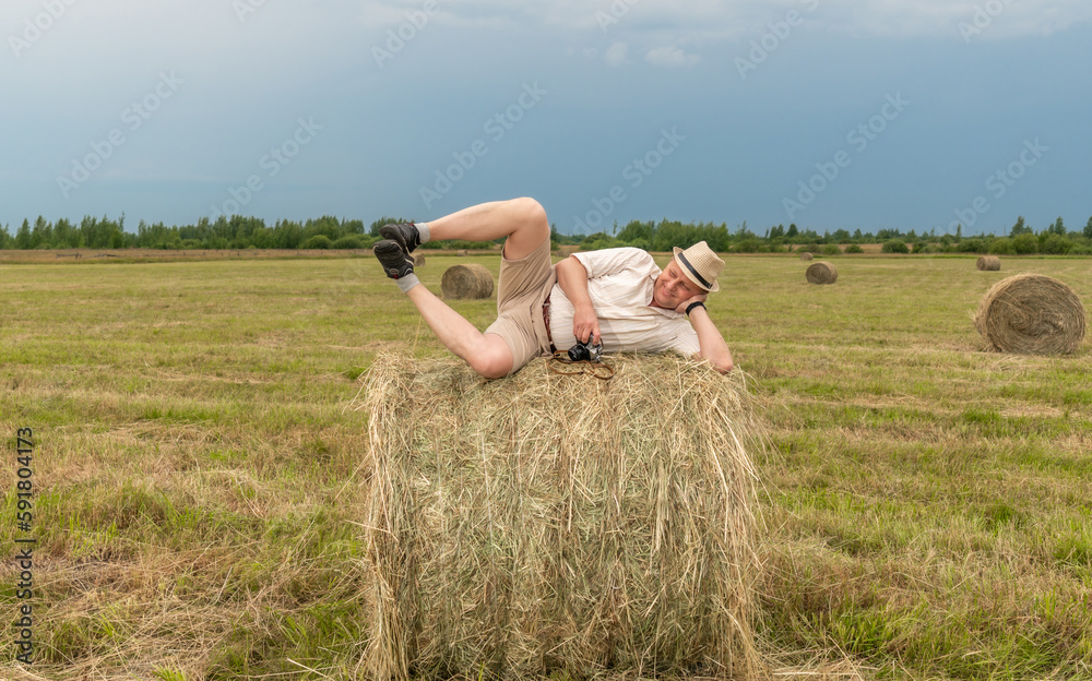 A man sitting on a large armful of straw in an empty field. Against the blue sky. A man sitting on a large armful of straw in an empty field. Against the blue sky.